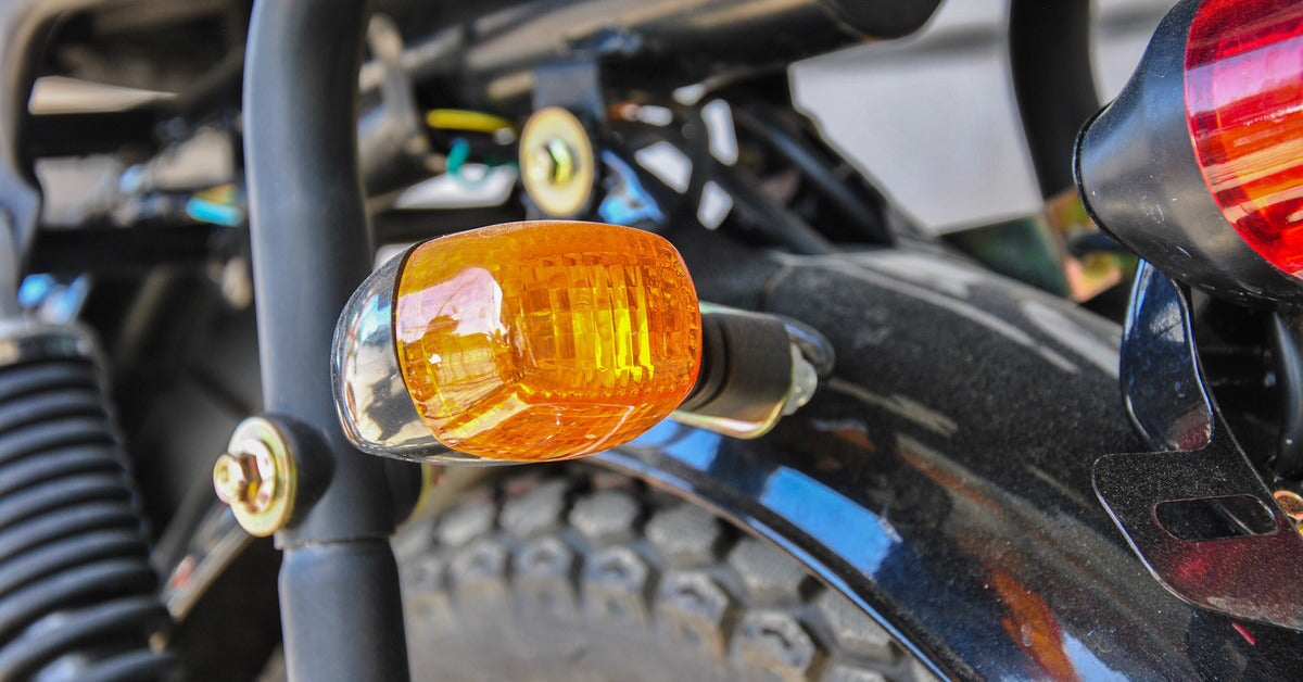 A close-up of a motorcycle's orange turn signal light. Part of the brake light can be seen on the frame's edge.