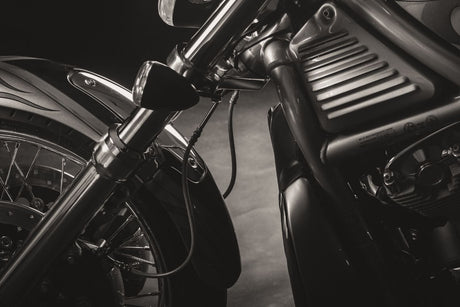 A closeup of a Harley V-Rod front end shows the front-wheel's cover, the twin forks, and headlights—all in black.