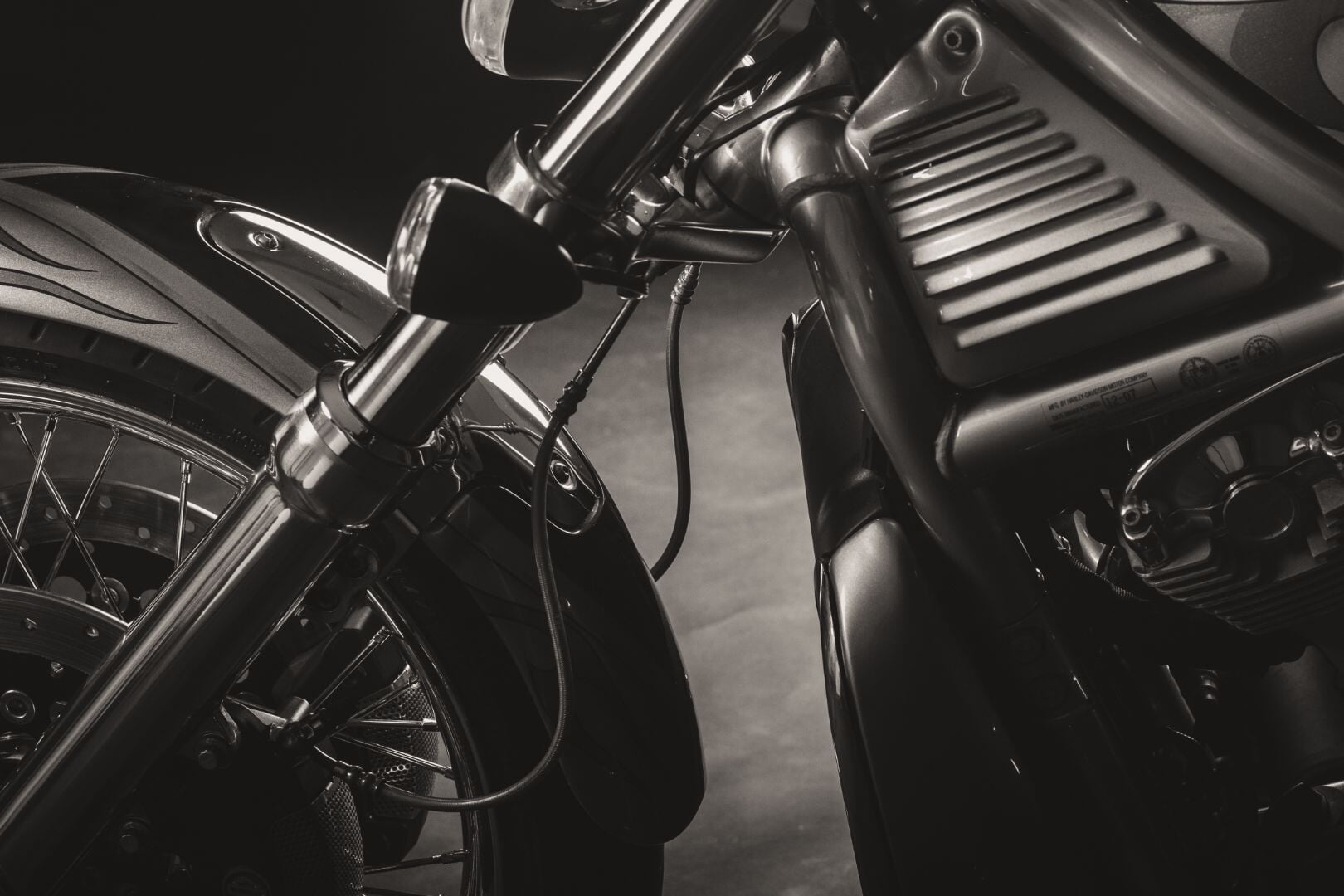 A closeup of a Harley V-Rod front end shows the front-wheel's cover, the twin forks, and headlights—all in black.