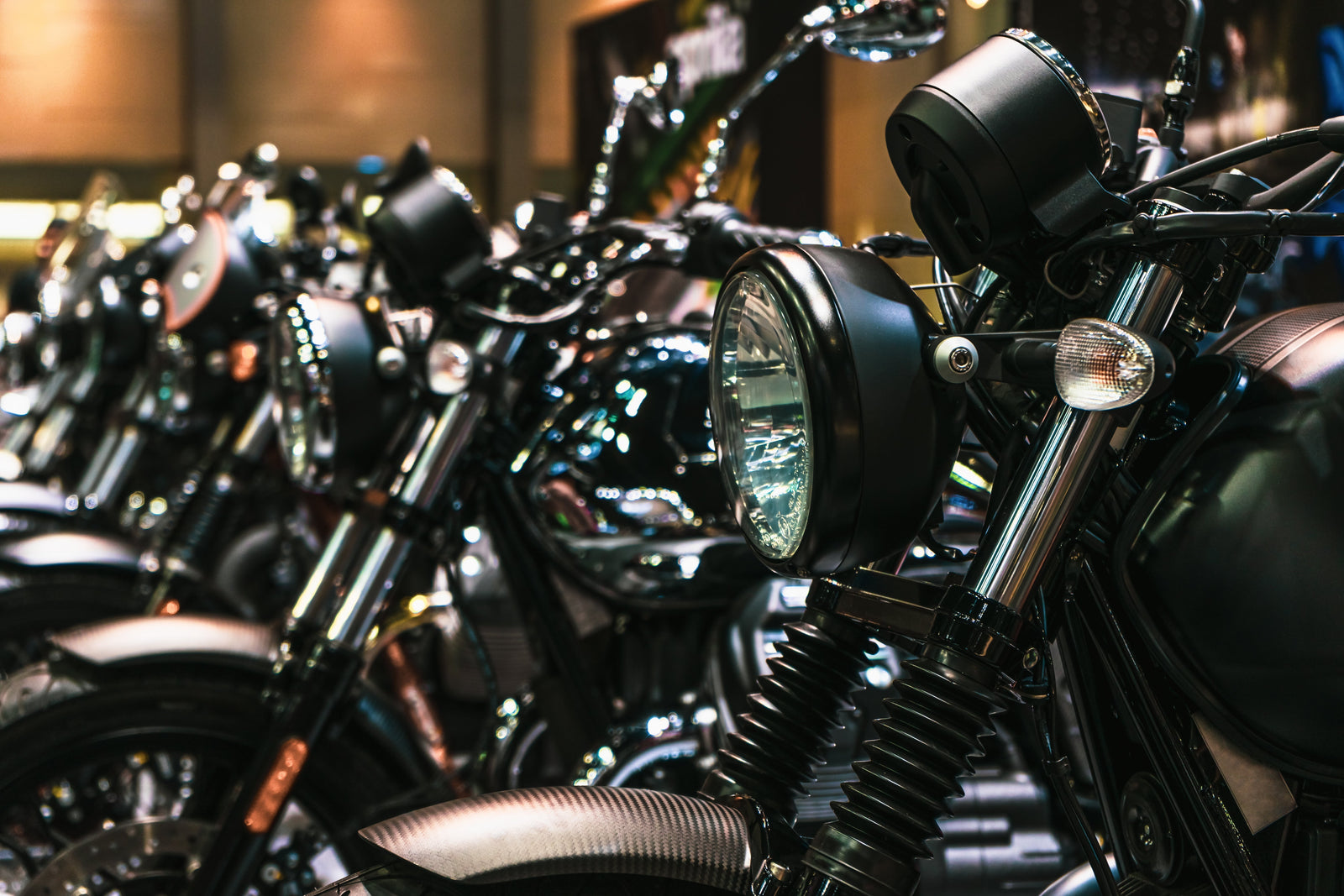 A close-up of a long row of darkly colored motorcycles with large, round headlights sitting inside a room.