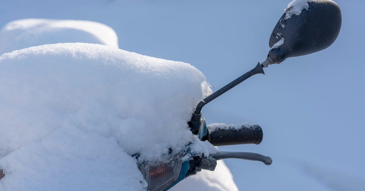 A parked motorcycle covered in a thick layer of snow. A headlight, a handlebar, and a mirror are free from the snow.