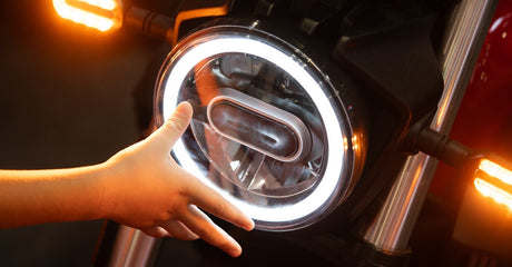 A person wearing a striped shirt touches the LED headlight on a bight red, silver and black motorcycle.